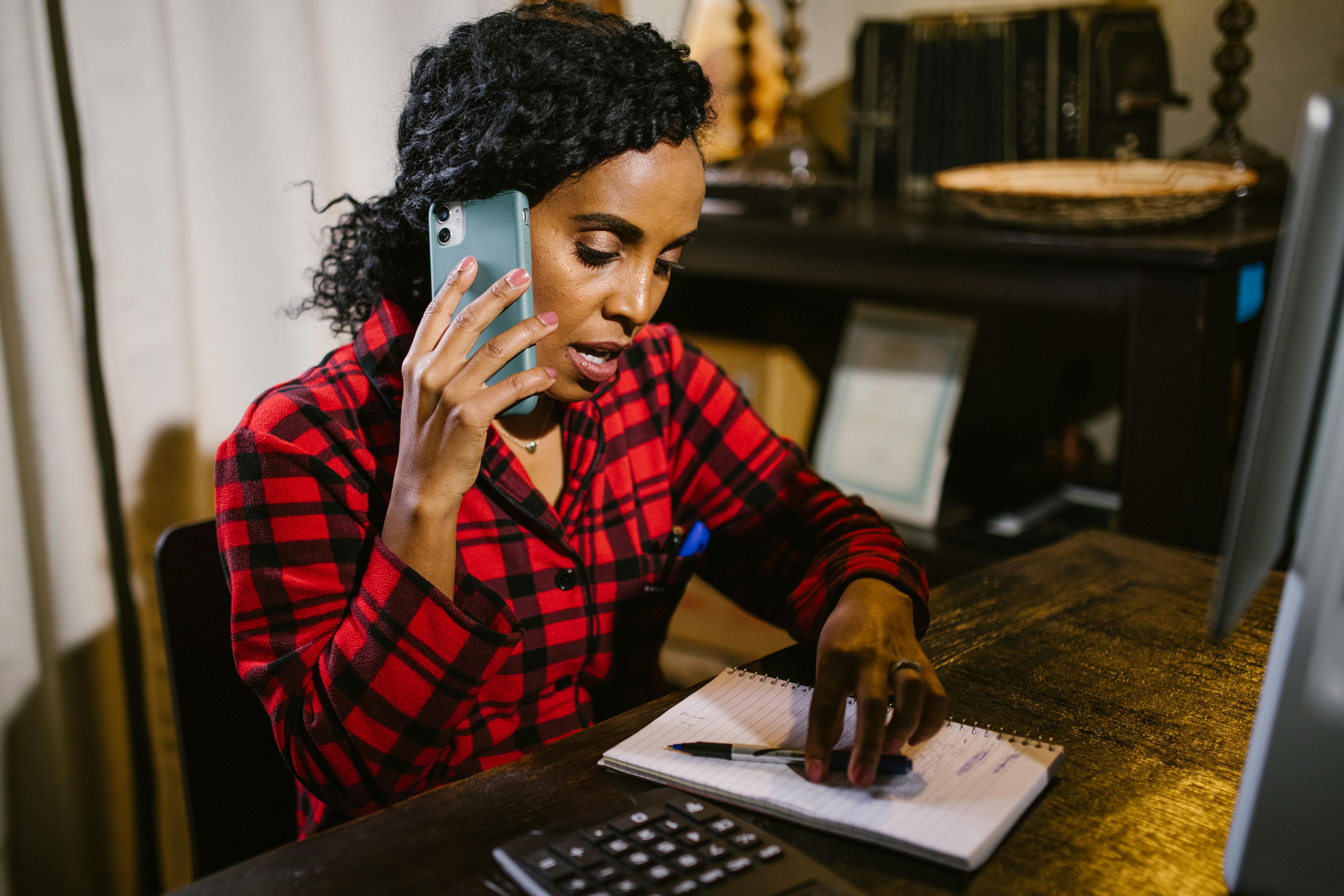 someone on the phone while looking at a notebook and sitting at a desk