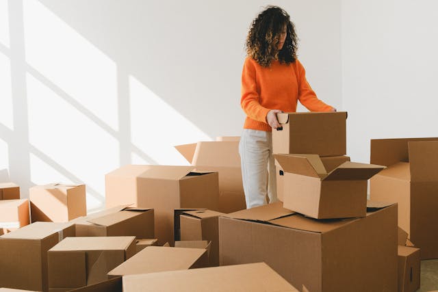 woman in orange sweater surrounded by brown moving boxes