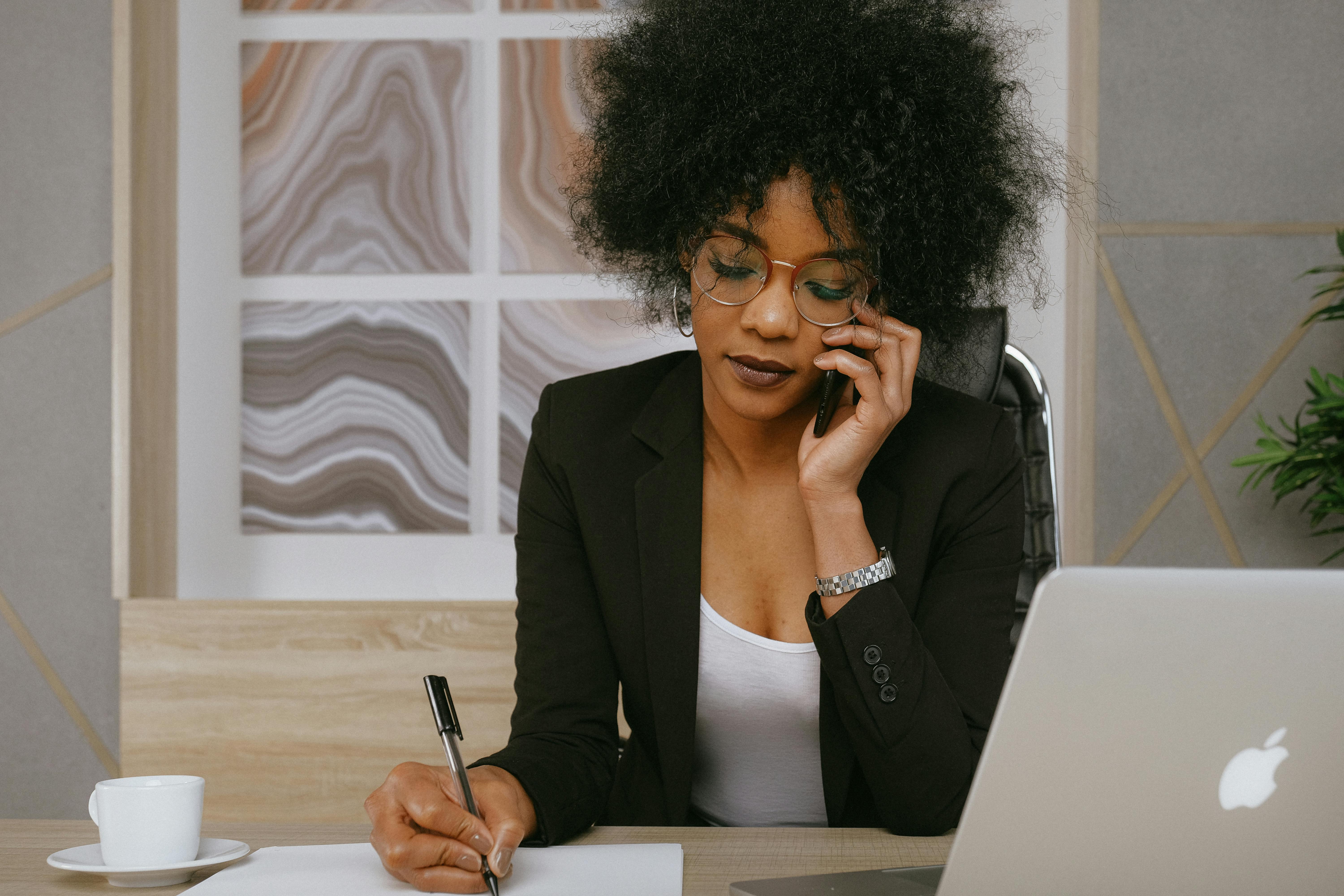 woman in blazer sitting at a desk and taking a phone call