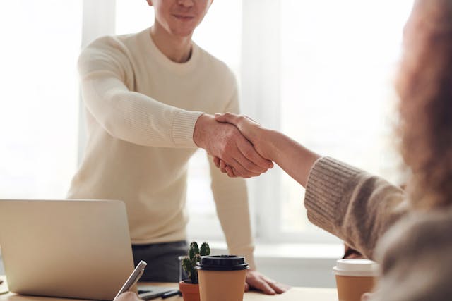 Two people in sweaters shake hands across a table