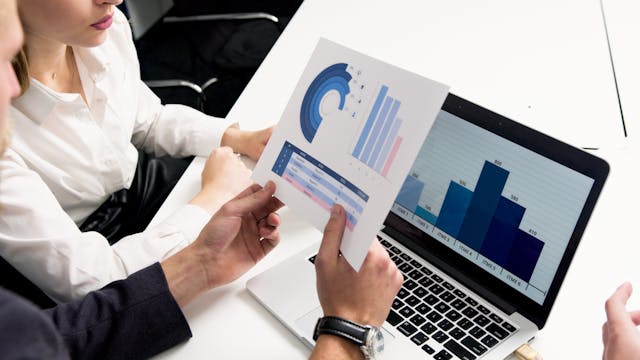 Two professionals reviewing printed charts and laptop graphs during a business meeting