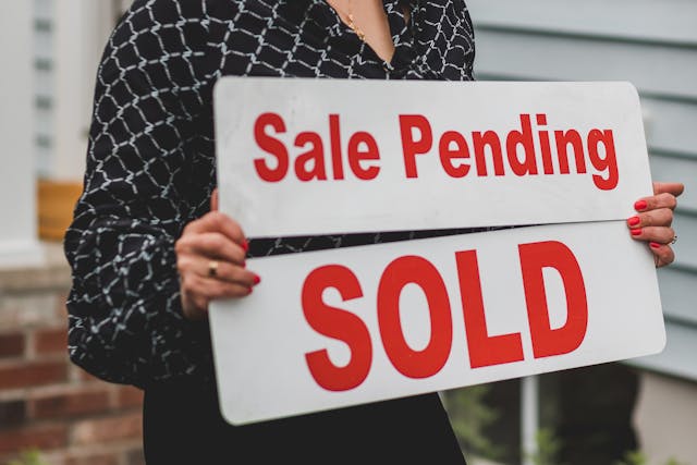 person holding two signs. One says "sale pending" and the other says "SOLD"